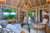 Tropical living room with wooden ceilings, rattan furniture, and open doors leading to a terrace with ocean views.