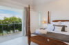 Bright bedroom with a wooden four-poster bed and open doors leading to a terrace with ocean views.