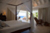Elegant bedroom with canopy bed opening to a private terrace and ocean view at Villa Plumbago, luxury St Barts villa rental.