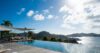 Infinity pool overlooking the ocean and rolling hills under a bright blue sky with scattered clouds