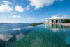Infinity-edge pool reflecting the sky, with a white pavilion overlooking the ocean and surrounding islands.