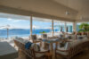 Spacious open living area with wooden furniture and neutral tones, overlooking an infinity pool and ocean views.