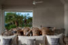 Elegant dining area with wicker chairs and neutral décor overlooking lush palm trees through large open windows