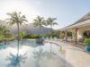 Sunlit lagoon-style pool framed by palm trees at a luxury St Barts villa, overlooking tropical hills and ocean light.