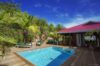 Sunlit private pool surrounded by tropical gardens and a red-roofed terrace at a St Barts villa rental.