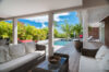 Shaded outdoor lounge with wicker sofas opening onto a sunlit deck and pool surrounded by tropical palms at a private St Barts villa