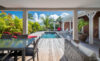 Covered terrace with dining and lounge area overlooking a private pool surrounded by palm trees at a luxury St Barts villa.